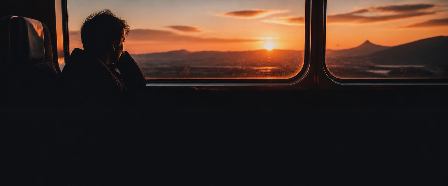 A traveller watching the landscape pass from a train window in golden light